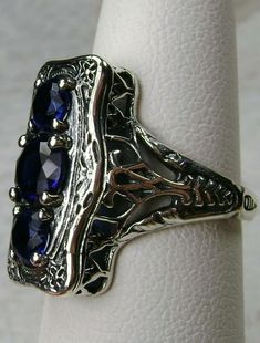 "Simulated Blue Sapphire Ring 3Stone Rectangle#60 Custom Made This is a lovely late Victorian era reproduction ring in solid sterling silver. The gorgeous filigree ring is set with 3 round-cut simulated blue sapphire gemstones. The 2 smaller blue sapphire gems are 4.5mm in diameter, and the center one is 6mm in diameter. This filigree setting is a casting from an actual Antique ring; notice the amazing etched band... The ring sits 3/4th\" (19mm) NS on the finger. The quality of the silver and ge Hallmarked Rings With Rectangular Stone For Anniversary, Rectangular Stone Hallmarked Rings For Anniversary, Rectangular Stone Ring Hallmarked For Anniversary, Vintage Silver Sapphire Ring With Emerald Cut, Elegant Oval Sapphire Ring Stamped 925, Vintage Sapphire Three Stone Ring For Formal Events, Vintage Three Stone Sapphire Ring For Formal Occasions, Sterling Silver Ring With Rectangular Stone For Formal Events, Vintage White Gold Sapphire Ring With Accent Stones