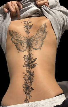 the back of a woman's body with flowers and a butterfly tattoo on it