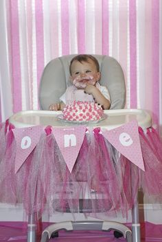 a baby sitting in a high chair with a pink cake on it's table