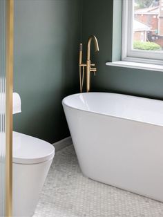 a white bathtub sitting next to a window in a bathroom with green walls and gold trim