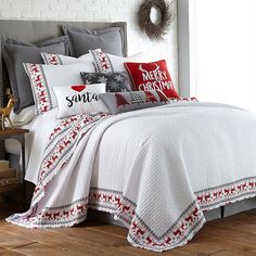 a white bed with red and gray pillows on it's sides, along with christmas decorations