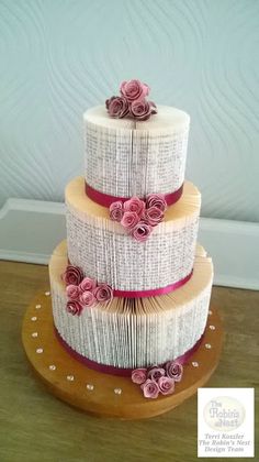 a three tiered cake with flowers on it sitting on a wooden table next to a wall