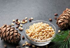 pine cones and nuts in a glass bowl on a black surface next to some pine needles