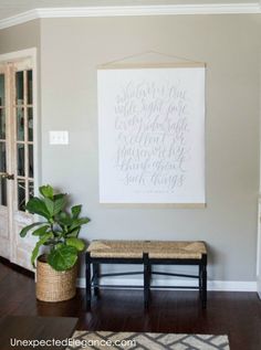 a living room with a bench, plant and large poster on the wall above it