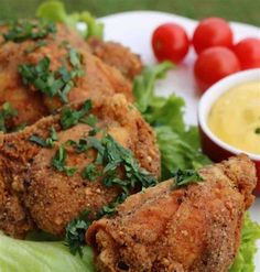 fried chicken with lettuce and tomatoes on a white plate next to dipping sauce