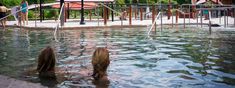 two women are sitting in the water at an outdoor swimming pool with umbrellas over them