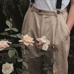 a man standing in front of flowers wearing suspenders