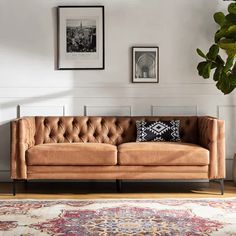 a tan leather couch sitting on top of a wooden floor next to a potted plant