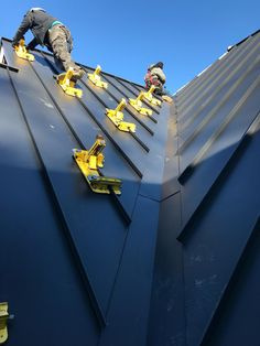 two men working on the roof of a building with metal shingles and yellow tools