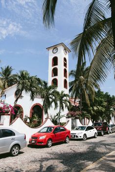 several cars parked in front of a building with a clock tower on it's side