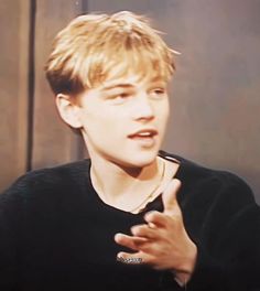 a young man with blonde hair talking to someone in front of him and wearing a black shirt