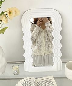 a woman taking a selfie in front of a mirror with an open book next to her