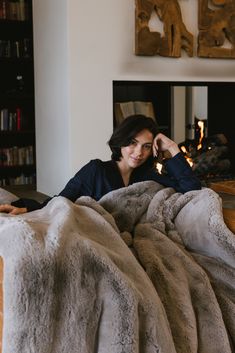 a woman laying on top of a couch under a blanket next to a fire place