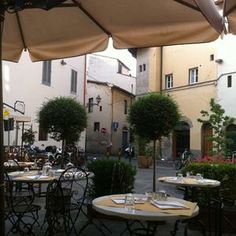 an outdoor dining area with tables, chairs and umbrellas in front of some buildings