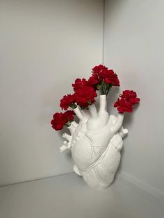 a white vase filled with red flowers sitting on top of a table next to a wall