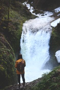 a person with a backpack is standing near a waterfall and looking down at the water