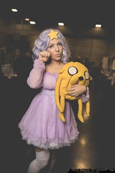 a woman in a purple dress holding a yellow stuffed animal and posing for the camera