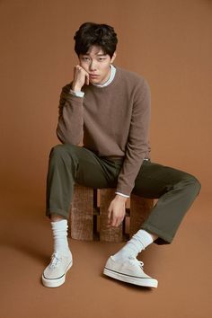 a young man sitting on top of a wooden crate wearing white sneakers and a brown sweater