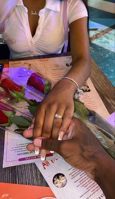 a man and woman sitting at a table with flowers in front of them, holding hands