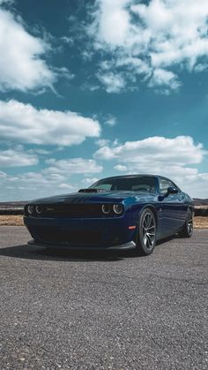 a blue sports car parked on the side of the road with clouds in the background