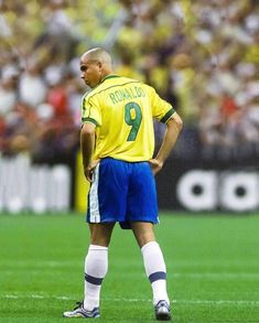 a man standing on top of a soccer field wearing a yellow shirt and blue shorts