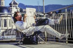 a man sitting in a chair reading a newspaper while holding his feet up to the ground