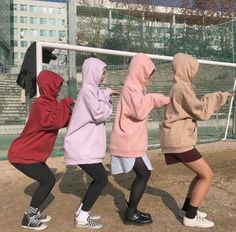 three girls in hoodies are playing with a soccer ball on a field near a fence