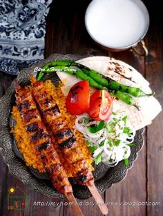 a plate filled with meat, rice and vegetables next to a glass of milk on a wooden table