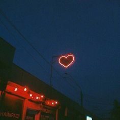 a neon heart sign is lit up in the dark sky above a storefront at night