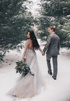 a bride and groom holding hands in the snow with pine trees behind them at their winter elopement