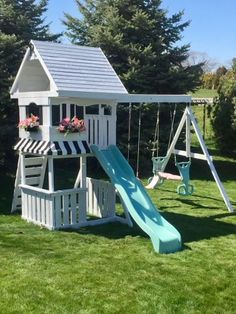 a wooden swing set with a blue slide and flower pots on the roof, next to green grass