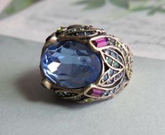 Here's a lovely size 5 (small), ring by Heidi Daus featuring a large blue oval stone, surrounded by colorful pavé set Swarovski crystals.  The four prongs holding the center stone are covered with amethyst baguettes, and the shoulders have a tulip flower design.  This ring is in exceptional vintage condition, with all stones present and no surface wear.  It is signed 'HEIDI DAUS' on the inside.  Jewelry by Heidi Daus is known for its superior quality, style and design, with all hand set stones and attention to detail.  The Miriam Haskell of her day, Daus's jewelry is extremely collectible and sought after, and is sold in the finest stores and boutiques, such as Harrod's of London, Bloomingdale's, and Saks.  Sorry, no original boxes.  Thanks for looking. Small Ring, Heidi Daus, Miriam Haskell, Tulip Flower, Oval Stone, Cocktail Ring, Blue Stone, Cocktail Rings, Flower Design