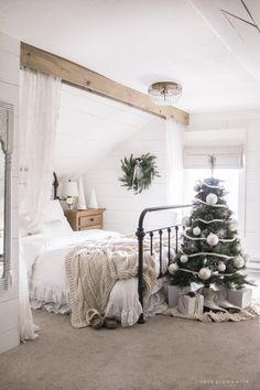 a bedroom decorated for christmas with a bed and a small tree in the corner next to it