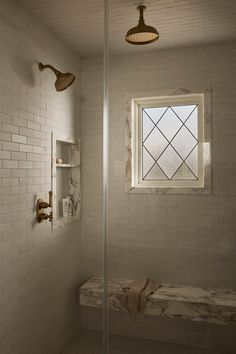 a white tiled bathroom with a window and bench in the corner, next to a shower head