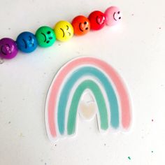 a rainbow with smiley faces on it next to colored beads and a sticker that says happy