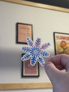 a person holding up a paper snowflake in front of pictures on the wall