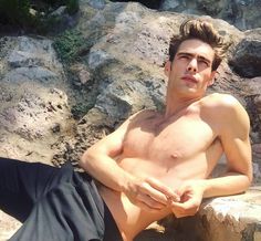 a shirtless young man sitting on top of a rock