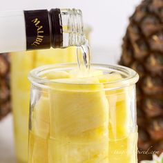 pineapple juice being poured into a jar with sliced pineapples in the background