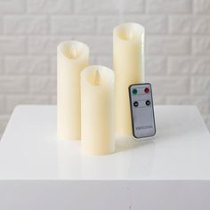 three white candles and a remote control on a table