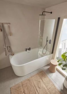 a white bathtub sitting next to a window in a bathroom with a rug on the floor