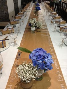 a long table with blue flowers in vases and place settings on the runner line