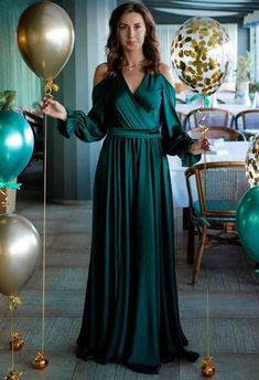 a woman in a long green dress standing next to balloons