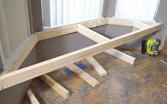 an unfinished bench sitting on top of a tile floor next to a pair of windows