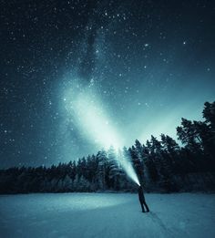 a person standing in the snow under a night sky filled with stars and bright lights