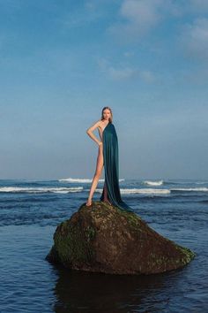 a woman standing on top of a rock in the ocean