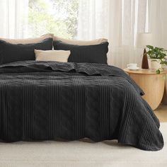 a bed with black comforter and pillows in a room next to a white rug