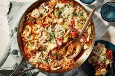 a pan filled with pasta and vegetables on top of a table next to two plates