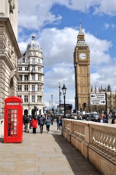 a red phone booth sitting on the side of a road next to tall buildings and a clock tower