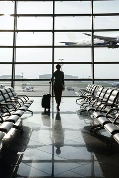 a woman walking through an airport terminal with her luggage in front of the window and planes on the tarmac behind her