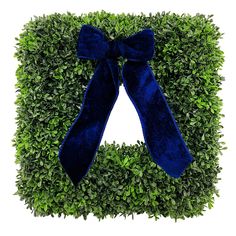 a square boxwood wreath with a blue bow on the top and green leaves around it